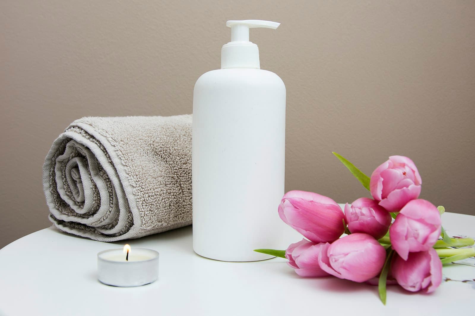 Toalla enrollada, vela y flores sobre una mesa de spa
